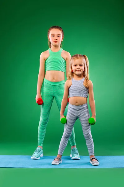 Дети девочки делают упражнения на зеленом фоне вместе — стоковое фото