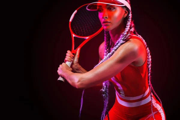 Giocatore di tennis. Bella atleta donna con racchetta in costume rosso e cappello isolato su sfondo nero. Concetto moda e sport . — Foto Stock