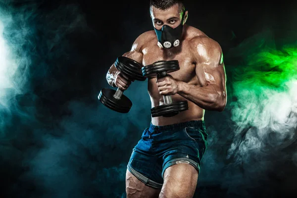 Muscular jovem homem de esportes fitness, fisiculturista em máscara de treinamento. Treino com haltere no ginásio de fitness — Fotografia de Stock