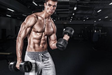 Atletik gömleksiz genç spor adamı - fitness modeli halter salonunda tutar. Kopya alanı metin ön plana.