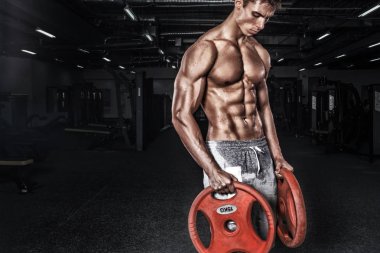 Atletik gömleksiz genç spor adamı - fitness modeli halter salonunda tutar. Kopya alanı metin ön plana.