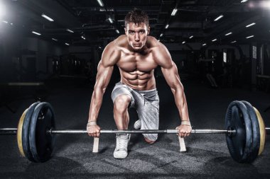 Atletik gömleksiz genç spor adamı - fitness modeli halter salonunda tutar. Kopya alanı metin ön plana.