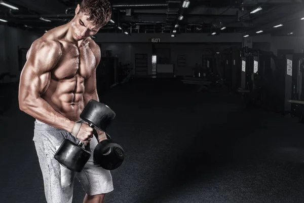 Athletic shirtless young sports man - fitness model holds the dumbbell in gym. Copy space fore your text. — Stock Photo, Image