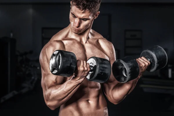 Athletic shirtless young sports man - fitness model holds the dumbbell in gym. Copy space fore your text. — Stock Photo, Image
