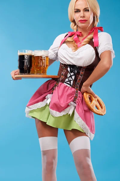 Ung sexig Oktoberfest tjej - servitris, bär en traditionell bayersk klänning, som serverar stora ölglas på blå bakgrund. — Stockfoto