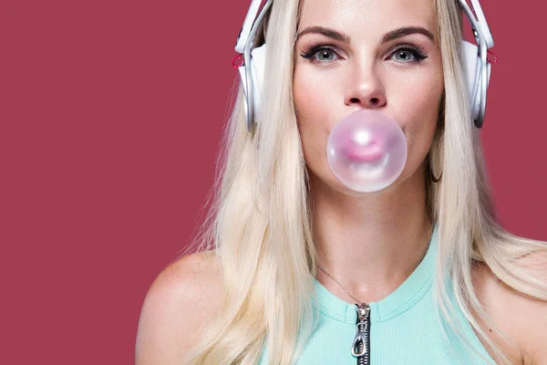 Bella donna bionda che soffia gomma da masticare rosa. Ragazza ascoltare musica in cuffia. Ritratto moda e lifestyle . — Foto Stock