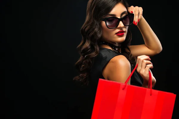 Viernes negro concepto de venta. Mujer de compras sosteniendo bolsa roja aislada sobre fondo oscuro en vacaciones —  Fotos de Stock