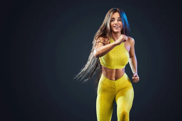 Forte atletica, velocista donna, corre su sfondo nero indossando l'abbigliamento sportivo giallo, fitness e motivazione sportiva. Concetto di corridore con spazio di copia . — Foto Stock