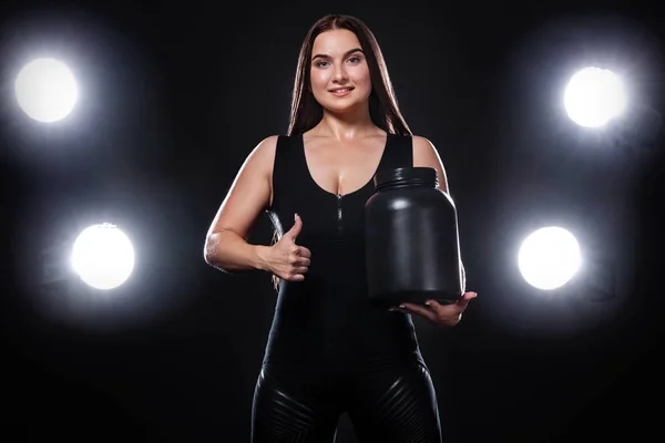 Atleta joven atleta deportiva de fitness muscular feliz y saludable con un frasco de nutrición deportiva: proteína, ganadora y caseína sobre fondo negro . — Foto de Stock