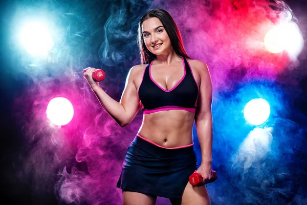 Größe plus Fitness-Sportlerin und Bodybuilderin mit Hantel auf schwarzem Hintergrund mit Licht und Rauch. — Stockfoto