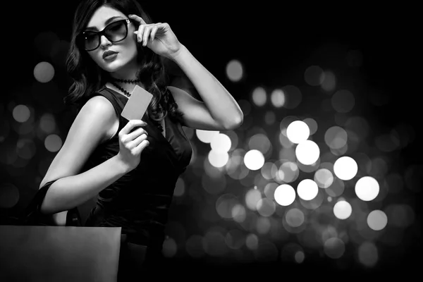 Jul eller svart fredag försäljning koncept. Shopping kvinna som håller påsen på mörk bakgrund med bokeh i semester. BW foto. — Stockfoto