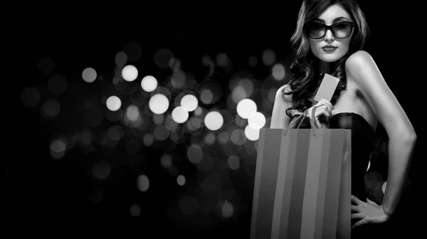 Christmas or Black friday sale concept. Shopping woman holding bag on dark background with bokeh in holiday. BW photo. — Stock Photo, Image
