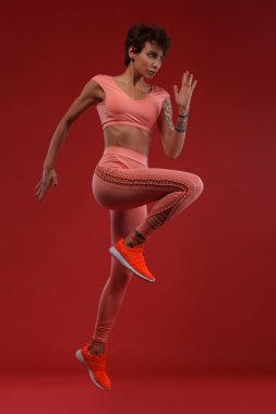 Bir güçlü atletik, kadın sprinter veya runner, spor giyim giymiş kırmızı zemin üzerine çalışan. Fitness ve spor motivasyon.