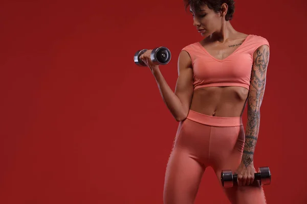 Mujer atleta en forma sosteniendo mancuerna. Concepto de fitness y motivación. Fondo rojo . — Foto de Stock