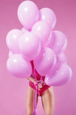 Renkli balonları olan güzel bir kız pembe arka planda gülüyor. Doğum günü partisindeki güzel mutlu genç kadın. Neşeli model eğleniyor, oynuyor ve pastel renkli balonla kutluyor.