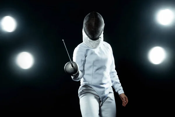 Szermierz młody sportowiec sobie kostium ogrodzenia, trzymając miecz i maskę. Na białym na czarnym tle z światła — Zdjęcie stockowe