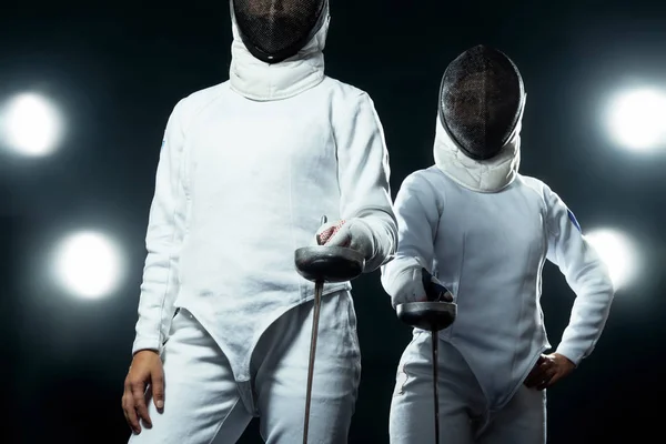 Αθλητής Ξιφασκίας νέων φορώντας μάσκα και λευκό περίφραξη κοστούμι. κρατώντας το σπαθί σε μαύρο φόντο με φώτα. — Φωτογραφία Αρχείου