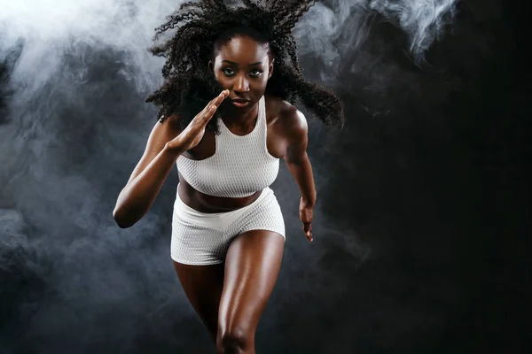 Fuerte atlético sprinter mujer de piel negra, corriendo sobre el fondo con el humo que lleva en la ropa deportiva. Fitness y motivación deportiva. Concepto de corredor con espacio de copia . —  Fotos de Stock