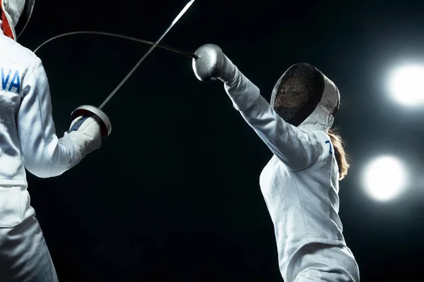 Szermierz młody sportowiec noszenie maski i biały kostium ogrodzenia. trzymając miecz na czarnym tle z światła. — Zdjęcie stockowe
