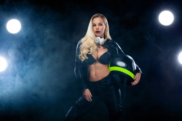 Modelo de moda DJ y motorista en auriculares, chaqueta de cuero negro, pantalones de cuero, mujer rubia bonita con estilo en traje informal noche. Peinado ondulado largo . — Foto de Stock