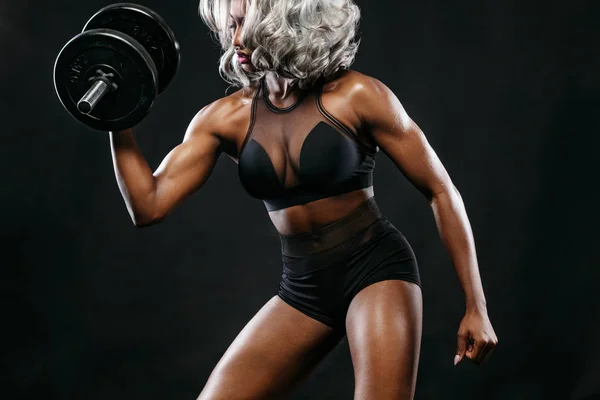 Deportiva hermosa mujer de piel negra con mancuernas hace ejercicio de fitness en el fondo oscuro para mantenerse en forma. Concepto deportivo . — Foto de Stock