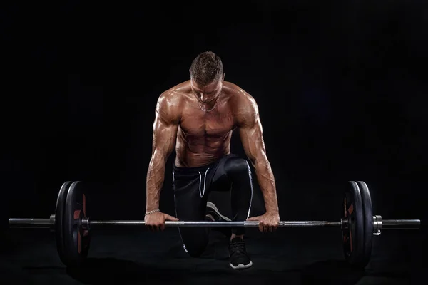 Foto de homem atlético musculoso forte fisiculturista bombeando os músculos com barbell no fundo preto. Conceito de musculação de energia de treino . — Fotografia de Stock