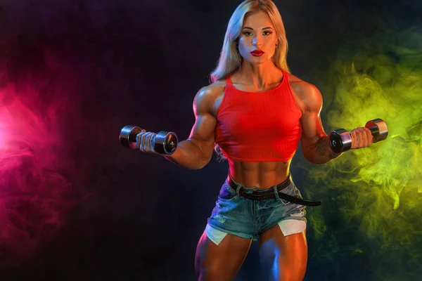 Güçlü atletik kadın vücut geliştirmeci şampiyon spor içinde giyen koyu arka plan üzerinde dumbbells ile. Fitness ve spor motivasyon. — Stok fotoğraf