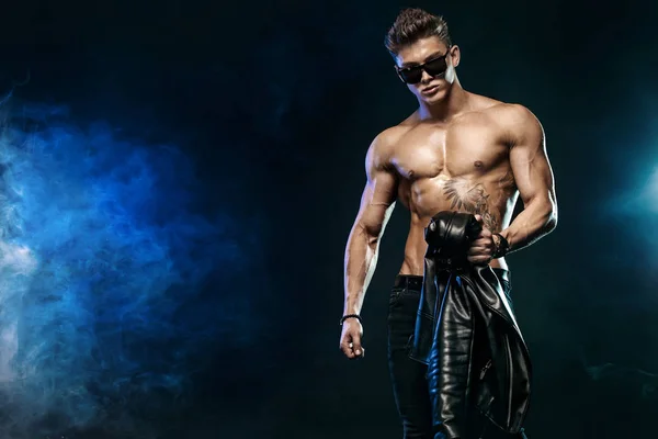 Moda uomo. Ritratto ravvicinato di un uomo brutale e in forma in topless con occhiali da sole e giacca di pelle. Atleta bodybuilder su sfondo nero . — Foto Stock