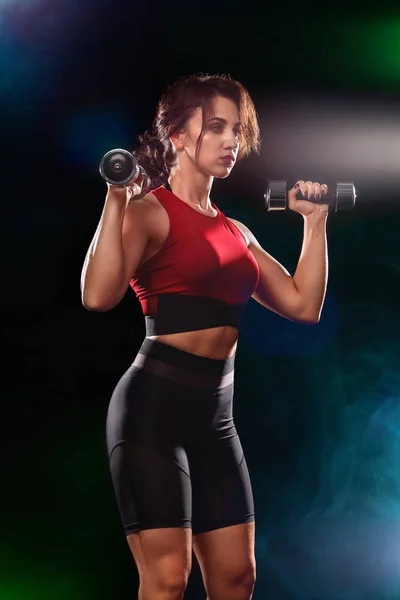 Sporty fit woman, athlete with dumbbells make fitness exercises on black background.