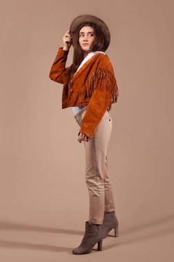 Moda kıyafetleri ve kahverengi arka planda şapka giyen bir kadın..