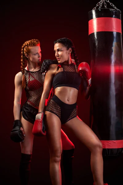 Dwa seksowne kobiety sportowca bokser robi szkolenia bokserskie na siłowni. Dziewczyna nosi rękawice, Odzież sportowa i uderza w worek do wykrawania. — Zdjęcie stockowe