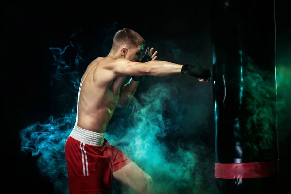 Sportsman, man Boxer slåss i handskar med boxning boxnings påse. Isolerad på svart bakgrund med rök. Kopiera utrymme. — Stockfoto