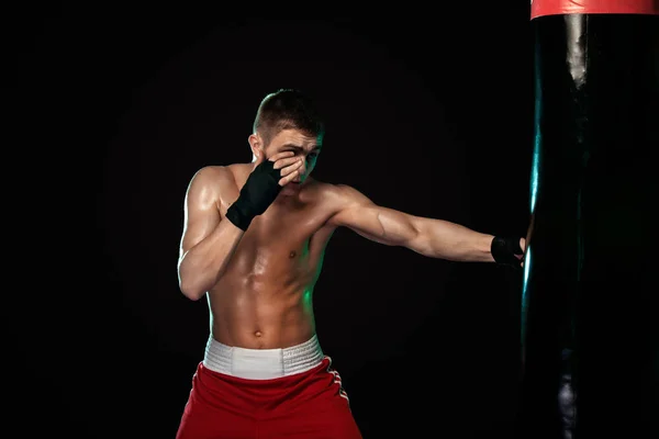 Deportista, hombre boxeador luchando con guantes con saco de boxeo. Aislado sobre fondo negro con humo. Copiar espacio . — Foto de Stock