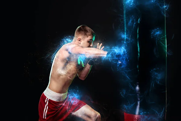 Deportista, hombre boxeador luchando con guantes con saco de boxeo. Aislado sobre fondo negro con humo. Copiar espacio . — Foto de Stock