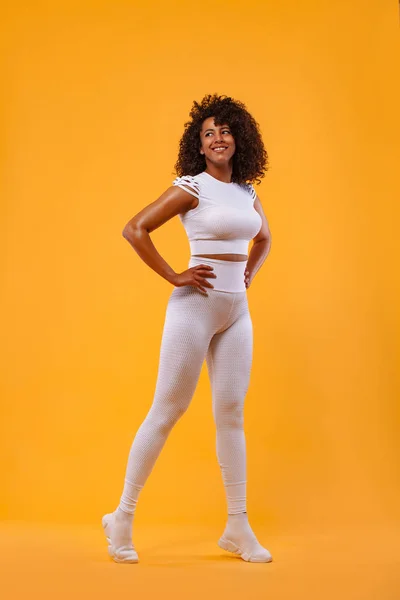 Sorridente donna atletica forte con pelle nera e capelli ricci, facendo esercizio su sfondo giallo indossando abbigliamento sportivo. Fitness e motivazione sportiva. — Foto Stock