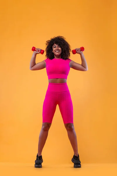 Sportig passform kvinna, idrottare med hantlar gör Fitness utövar på gul bakgrund. Fitness och workour motivation. — Stockfoto