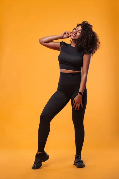 Concepto de estilo de vida. Retrato de una hermosa mujer afroamericana con el pelo rizado alegre escuchando música en el teléfono móvil. Fondo amarillo del estudio. Copiar espacio . — Foto de Stock