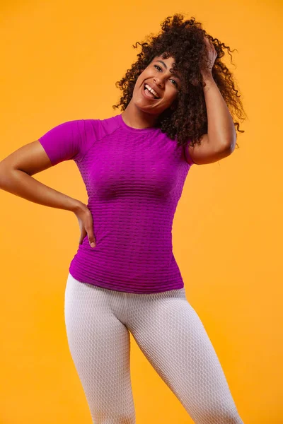 黒い肌と巻き毛を持つ強い運動能力の女性を笑顔、スポーツウェアを着て黄色の背景に運動を行う。フィットネスとスポーツの動機. — ストック写真