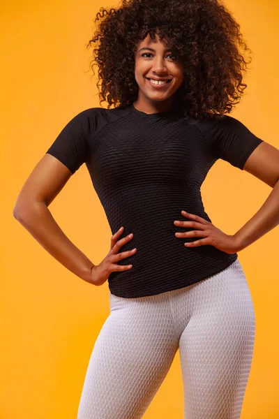 Lachende sterke atletische vrouw met zwarte huid en krullend haar, doen oefening op gele achtergrond dragen sportkleding. Fitness en sportieve motivatie. — Stockfoto