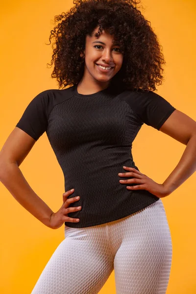 Mosolygó erős sportos nő fekete bőr és göndör haj, gyakorló sárga háttér visel sportruházat. Fitnesz és sportmotiváció. — Stock Fotó