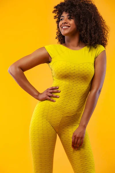 黒い肌と巻き毛を持つ強い運動能力の女性を笑顔、スポーツウェアを着て黄色の背景に運動を行う。フィットネスとスポーツの動機. — ストック写真