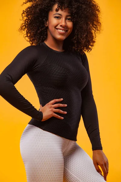 Lachende sterke atletische vrouw met zwarte huid en krullend haar, doen oefening op gele achtergrond dragen sportkleding. Fitness en sportieve motivatie. — Stockfoto