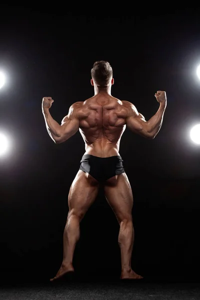 Ισχυρή μυϊκή bodybuilder αθλητή άνθρωπος που θέτουν και την άντληση των μυών σε μαύρο φόντο. Προπόνηση bodybuilding ιδέα. — Φωτογραφία Αρχείου