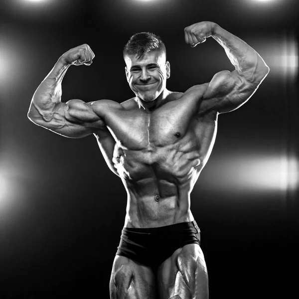 Zwart-wit foto. Sterke gespierde bodybuilder atleet man poseren en oppompen spieren op donkere achtergrond. Training Bodybuilding concept. — Stockfoto