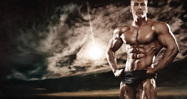 Fuerte musculoso atleta atleta hombre posando y bombeando los músculos al aire libre. Concepto de culturismo de entrenamiento . — Foto de Stock