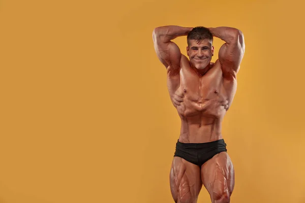 Acımasız güçlü kas vücut geliştirmeci atlet adam sarı arka plan üzerinde kasları pompalama. Egzersiz vücut geliştirme konsepti. — Stok fotoğraf