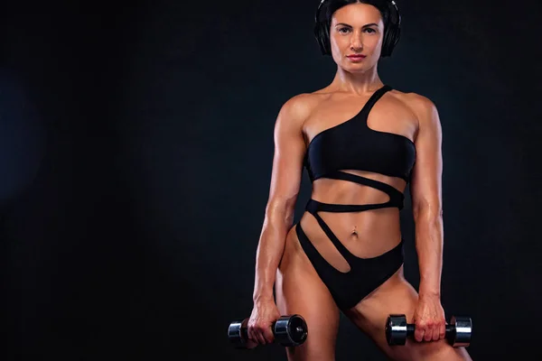 Sterke gespierde bodybuilder atletische vrouw oppompen spieren met dumbbells op zwarte achtergrond. Training Bodybuilding concept. — Stockfoto