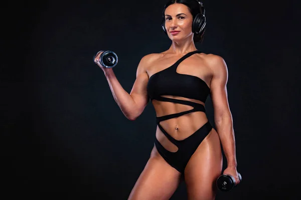 Forte bodybuilder muscolare donna atletica pompaggio muscoli con manubri su sfondo nero. Allenamento concetto di bodybuilding . — Foto Stock