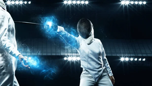 Two fencers on professional sports arena. Young athletes wearing mask and white fencing costume on duel in action. Women holding the sword on black background with lights. — Stock Photo, Image