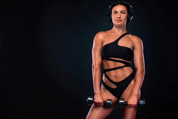 Forte bodybuilder muscolare donna atletica pompaggio muscoli con manubri su sfondo nero. Allenamento concetto di bodybuilding . — Foto Stock